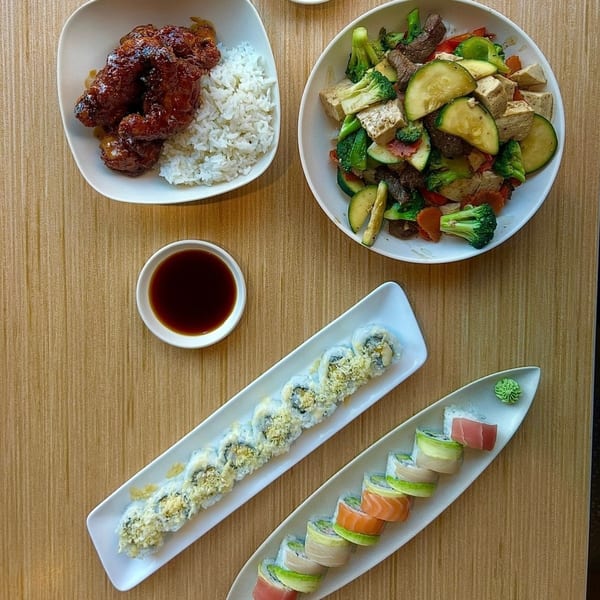 An overhead view of various Asian dishes, including sushi rolls, stir-fry, and chicken with rice.
