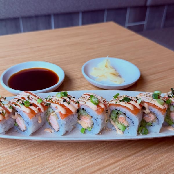 A plate of salmon sushi rolls with spicy mayo, green onions, and sesame seeds, with soy sauce and ginger.
