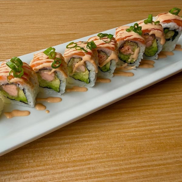 Salmon and avocado sushi rolls topped with spicy mayo and green onions on a white plate.