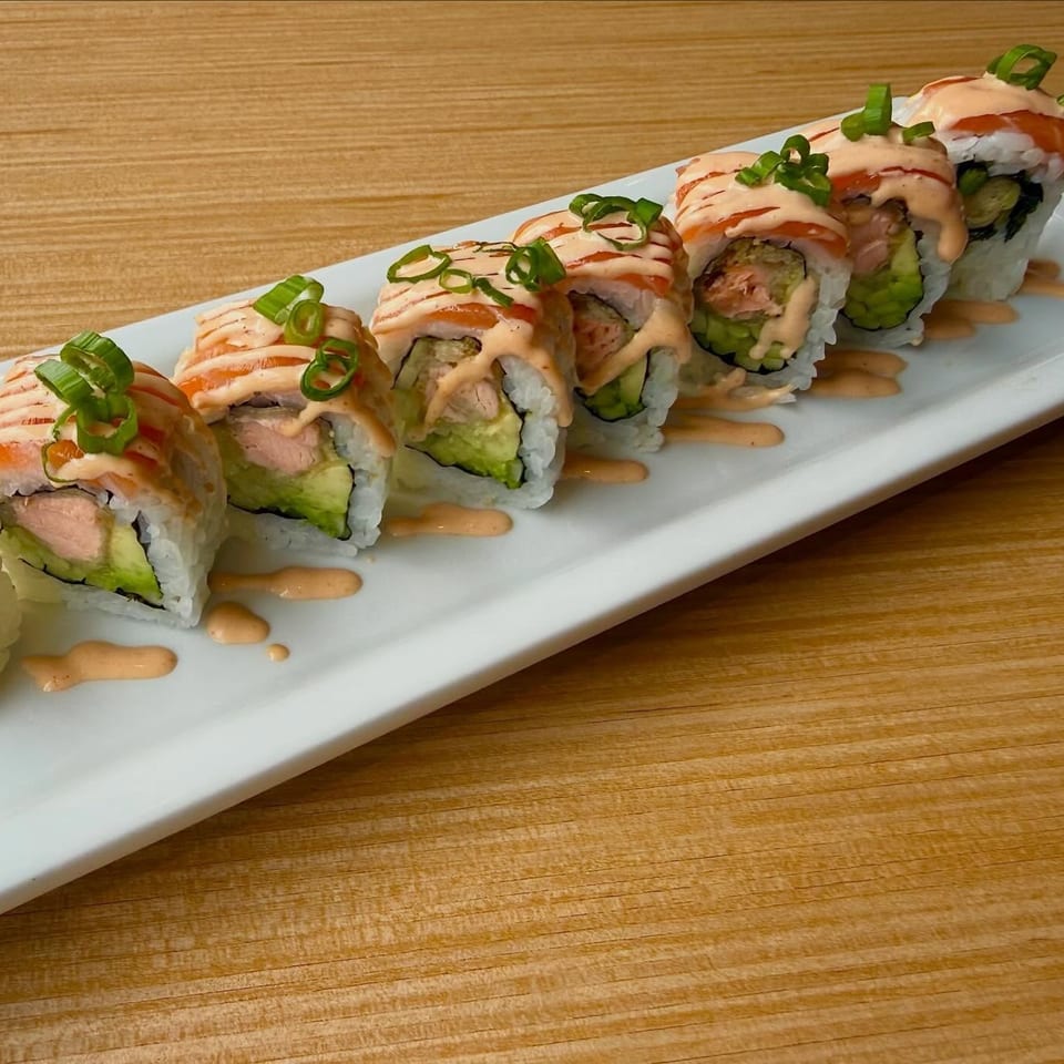 Salmon and avocado sushi rolls topped with spicy mayo and green onions on a white plate.