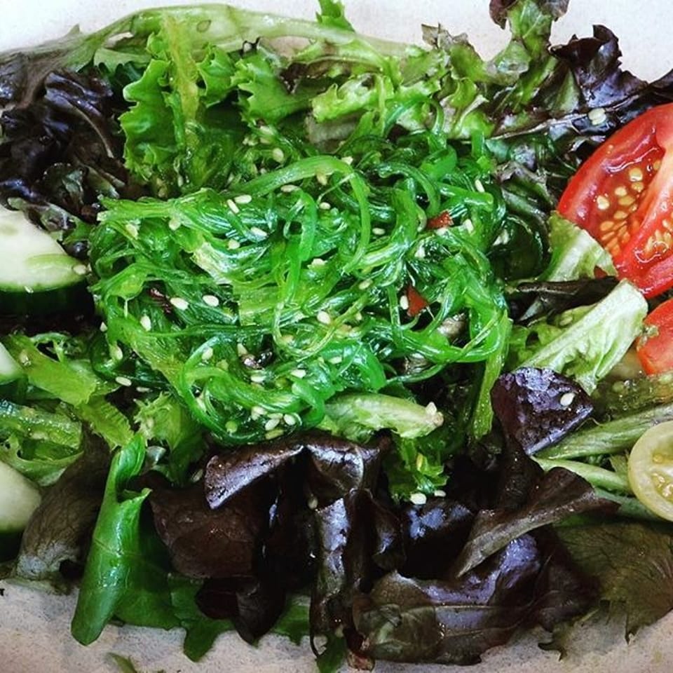 Vibrant green seaweed salad with sesame seeds, mixed greens, cucumber, and sliced tomatoes.