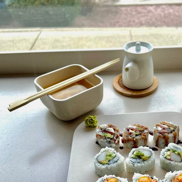 Assorted sushi rolls, including California and eel, with wasabi, soup, and a soy sauce dispenser by a window.