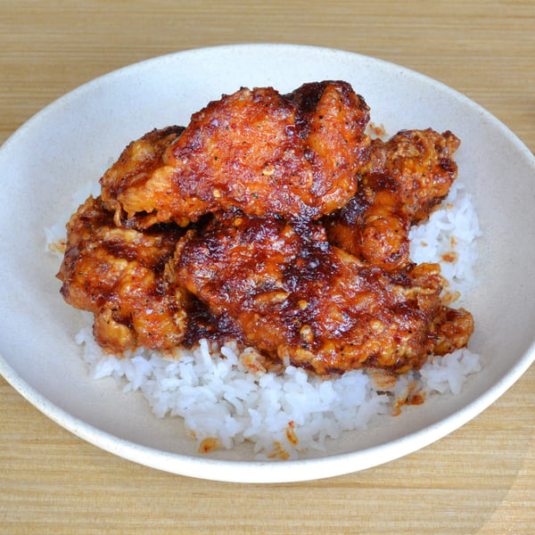 Crispy fried chicken wings coated in a spicy red sauce, served over white rice with chopsticks.
